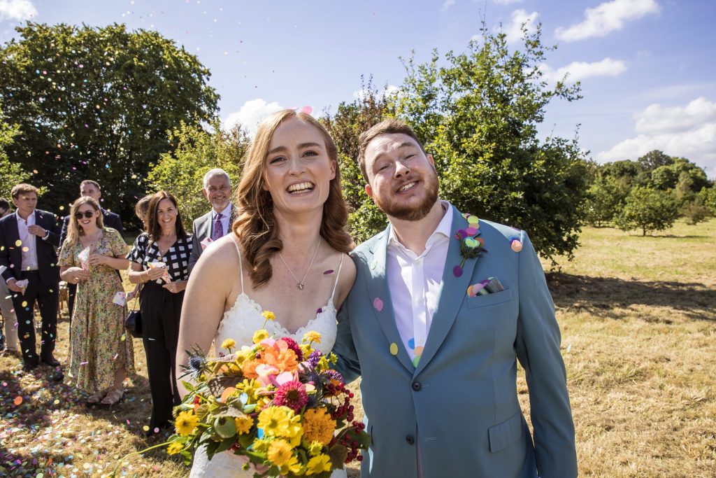 new husband and wife at their garden wedding in hertfordshire. photographer captures a smile between happy couple with summer flowers